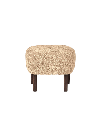 Side view of the Ingeborg Ottoman with a plush, honey-coloured sheepskin seat and short, dark-stained oak legs.