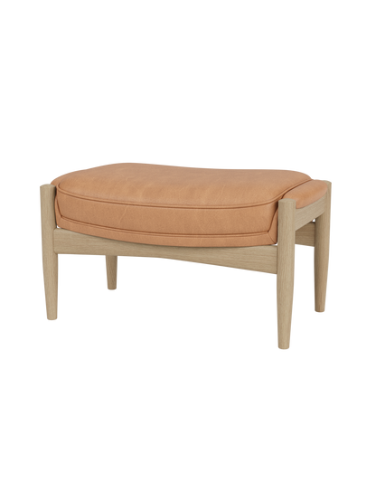 The Seal Ottoman featuring a tan Dunes leather cushion and a natural oak wood frame with sculpted mid-century legs.