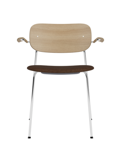 Co Dining Chair with chrome armrests, a natural oak backrest and a dark bouclé upholstered seat.