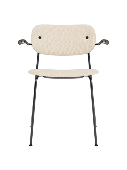 Co Dining Chair with armrests featuring Logan Jasmine cream upholstery and dark stained oak on a black steel base.