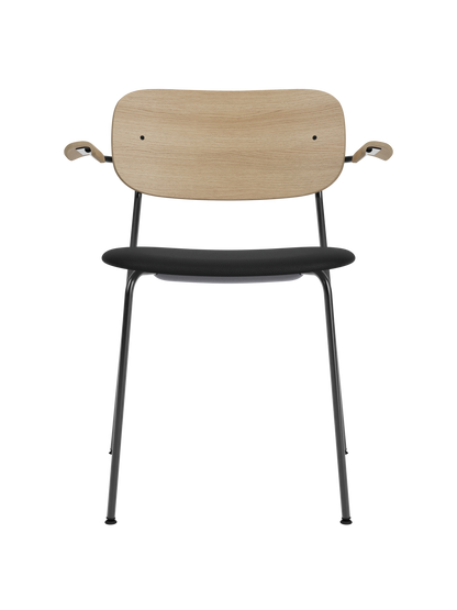 Co Dining Chair with armrests, natural oak backrest and black upholstered seat on a minimalist black steel frame.