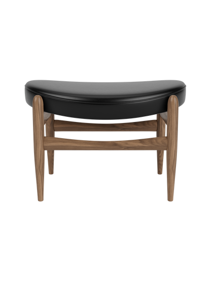 Elizabeth Ottoman featuring a curved black leather seat and an elegant walnut frame by Ib Kofod-Larsen.