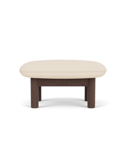 Side view of the Brasilia Ottoman with a dark stained oak frame and a light, textured Logan Jasmine fabric cushion.