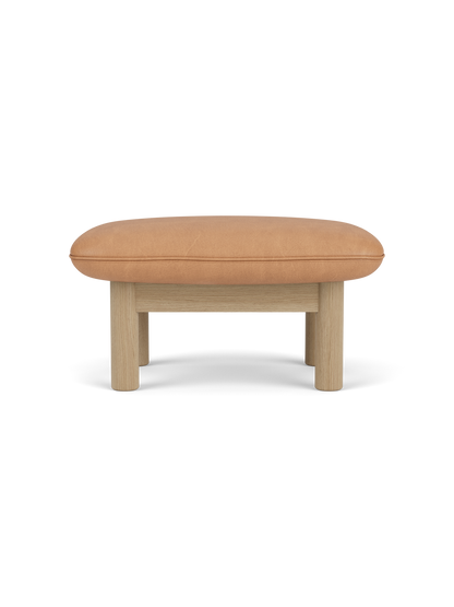 Side view of the Brasilia Ottoman with a camel leather cushion and a natural oak frame with four robust, cylindrical legs.