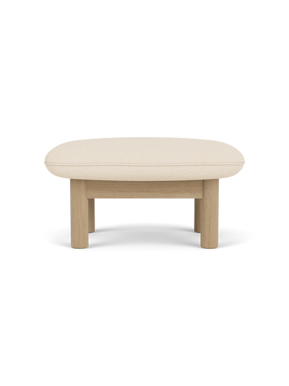 A side view of the Brasilia Ottoman with a natural oak frame and a light beige Logan Jasmine cushion on a black background.