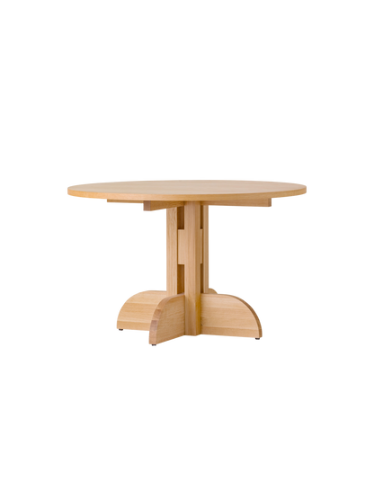 Puffin Dining Table, Round, in natural oak with a sculptural solid wood base, shown at an angle against a white background.