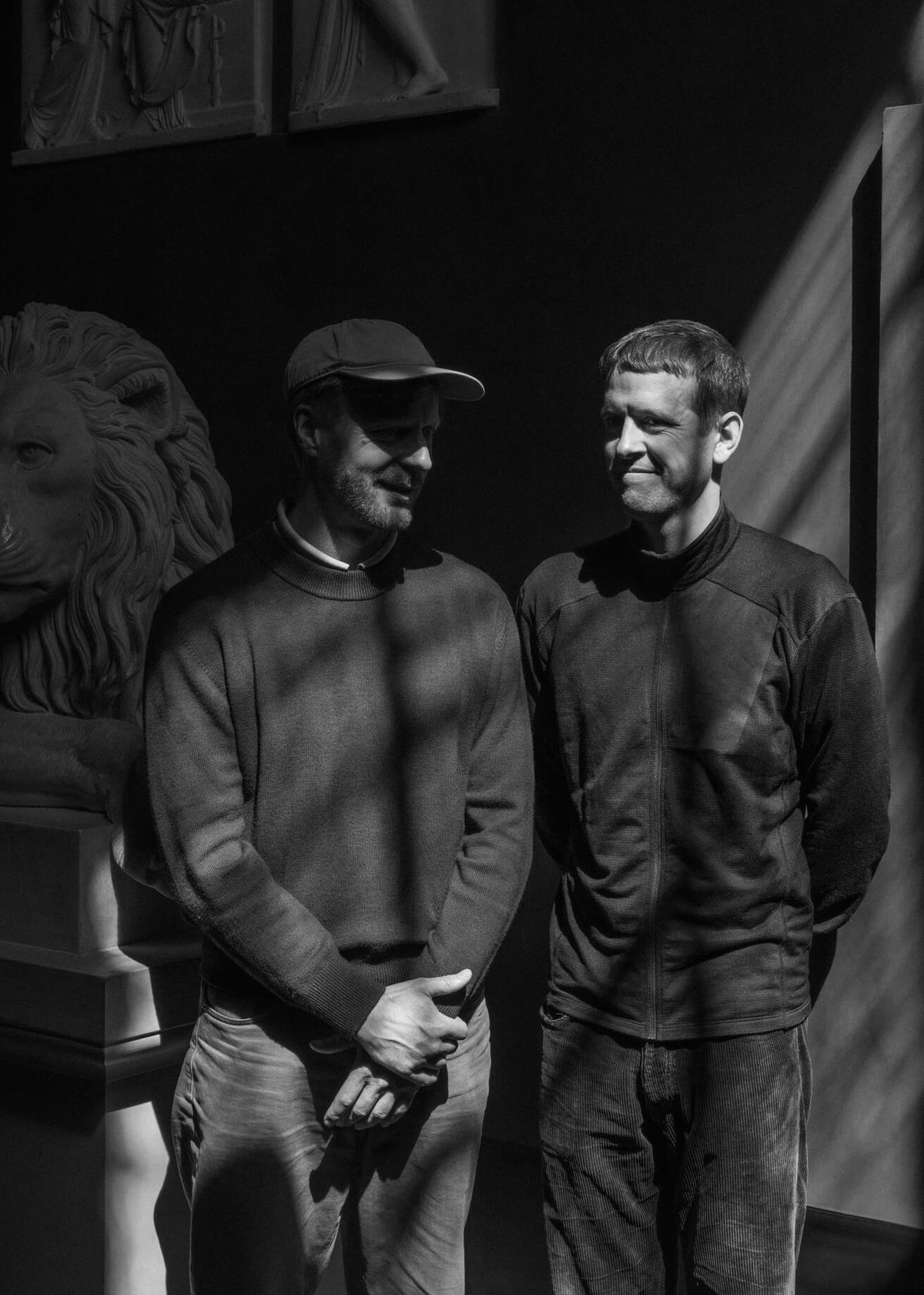 Two men standing together in a museum gallery next to classical sculptures in this black and white portrait for Audo CPH.
