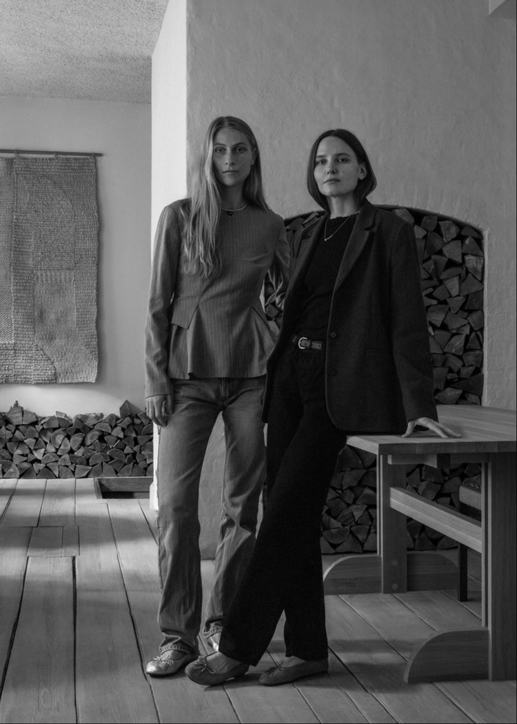 Two women posing next to an Axo table in an Audo Atelier interior space with wooden flooring and a textured wall.