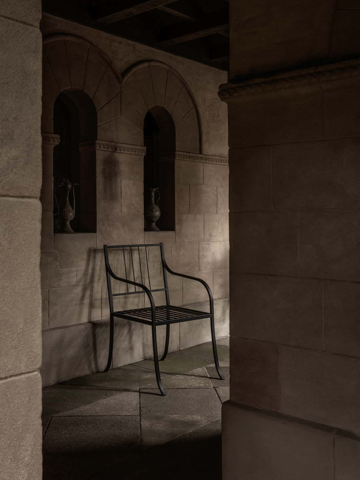 Bloss Garden Dining Chair in black powder-coated steel within an atmospheric stone alcove with arched architectural details.