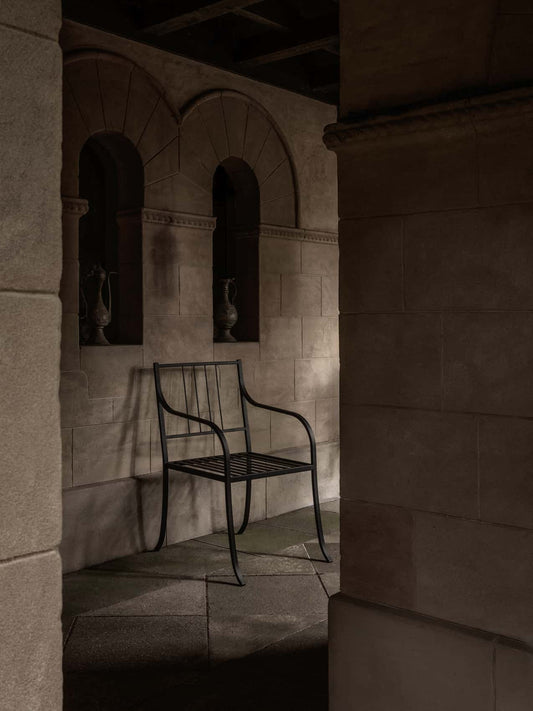 Bloss Garden Dining Chair in black powder-coated steel within an atmospheric stone alcove with arched architectural details.