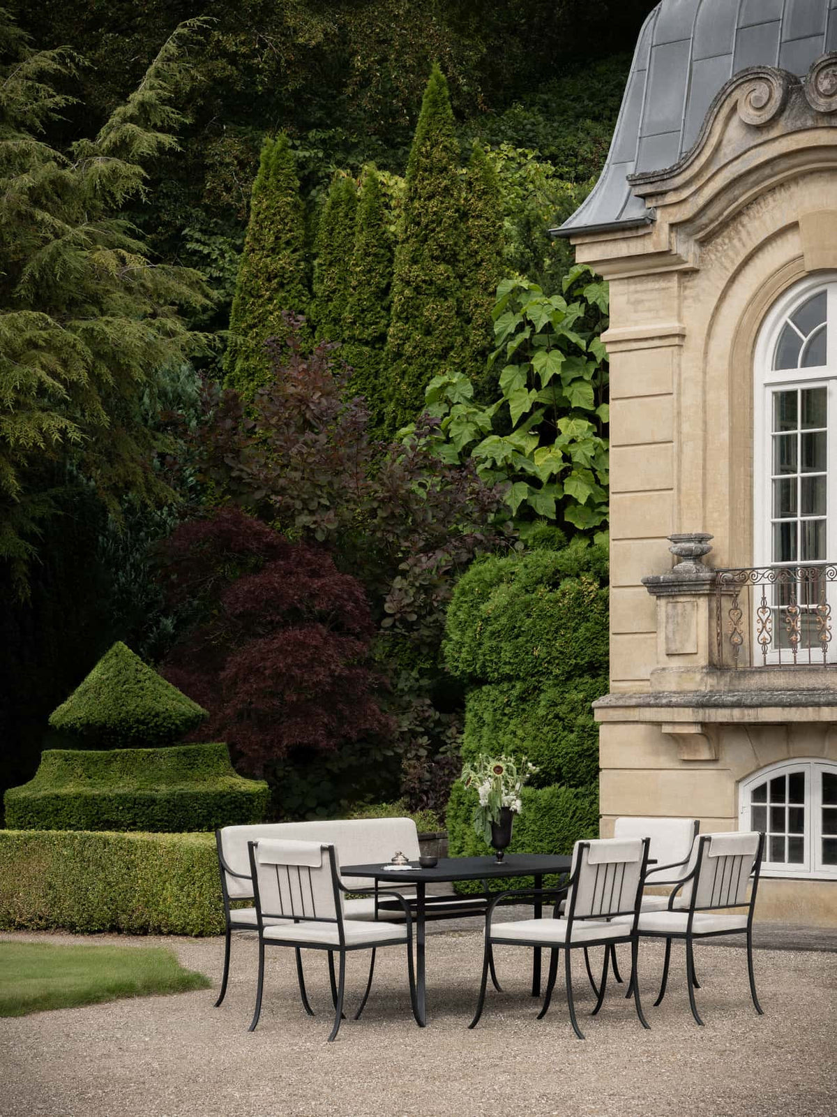 Bloss Garden Dining Table paired with chairs, bench cushion set and Pavot Vase in an outdoor garden setting.