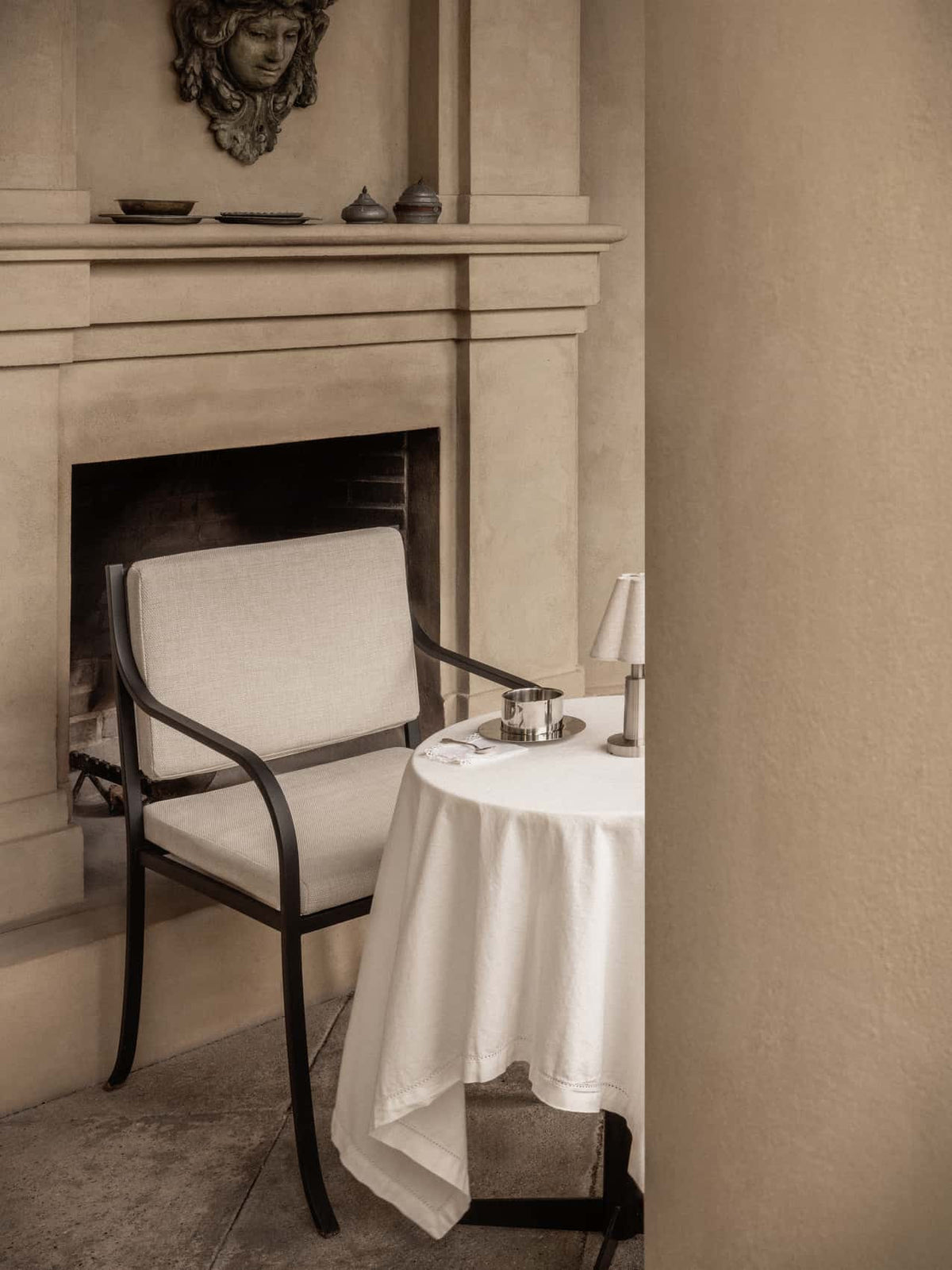 Bloss Garden Dining Chair with cushion set near a small round table with a portable lamp and classic fireplace.