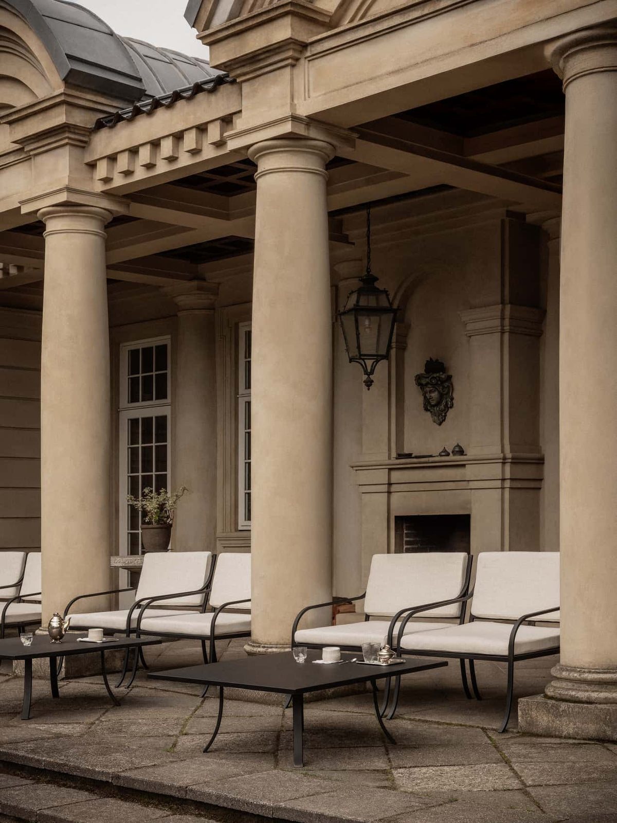 Bloss Garden Lounge Table in black powder-coated steel paired with lounge chairs under a classical columned porch.