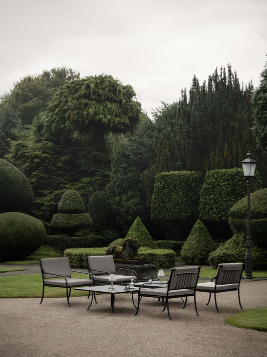 Bloss Garden Lounge Table and chairs with cushions in a green garden, with an Admiral Portable Lamp.