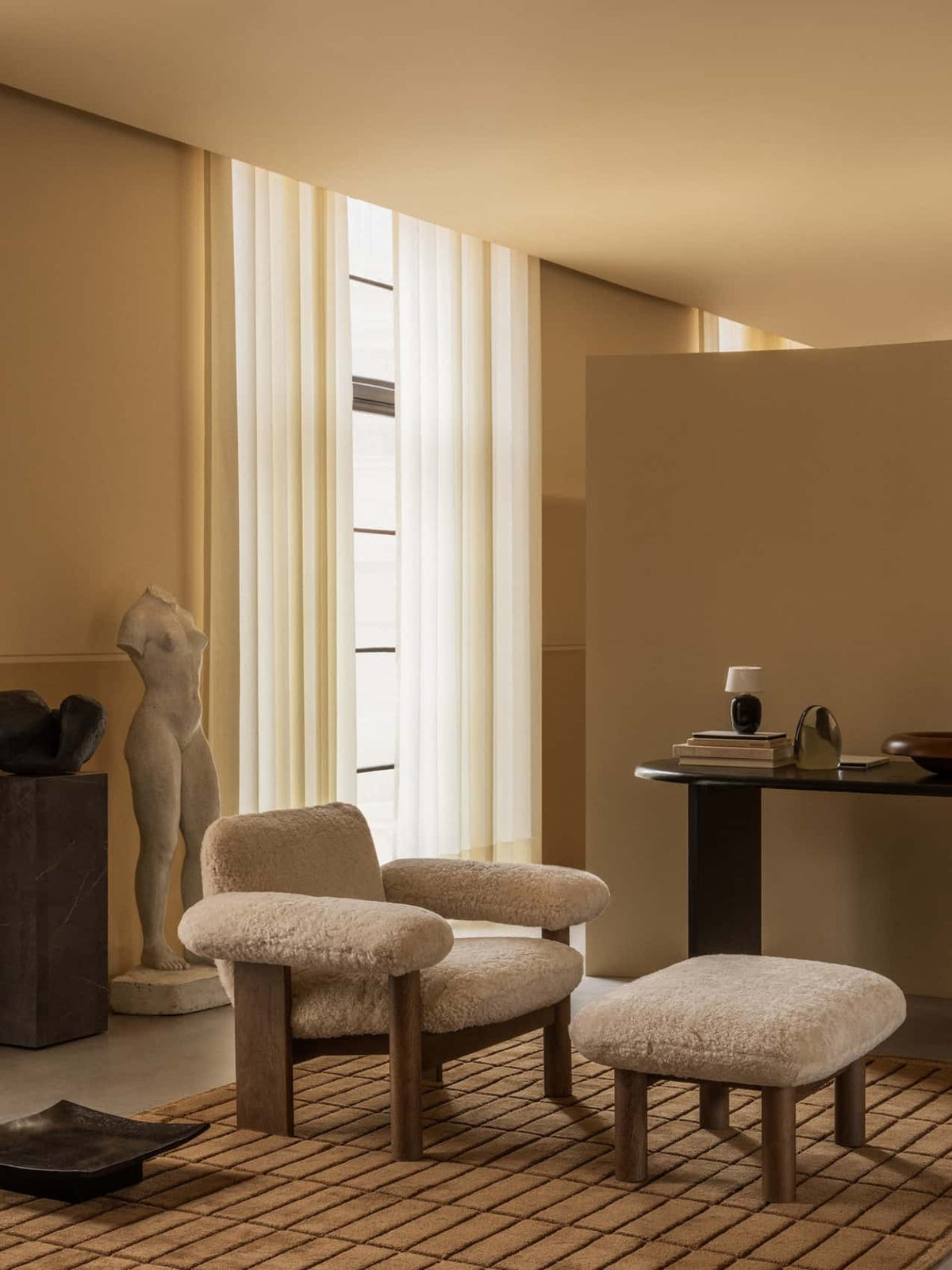 Brasilia Ottoman and Lounge Chair in soft sheepskin with wooden legs, placed in a warm interior on a tile rug.