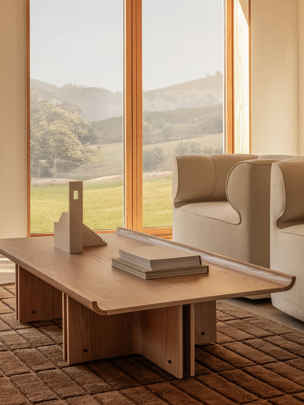 Wooden Conrad Lounge Table and beige Eave Seamline Lounge Chair on a textured brown Tile Rug by a large window.