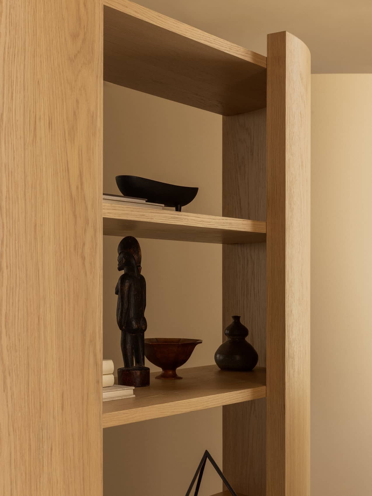 Close-up of Audo Crescent Shelving in light oak, styled with a dark wood sculpture, ceramic vases, and decorative bowls.