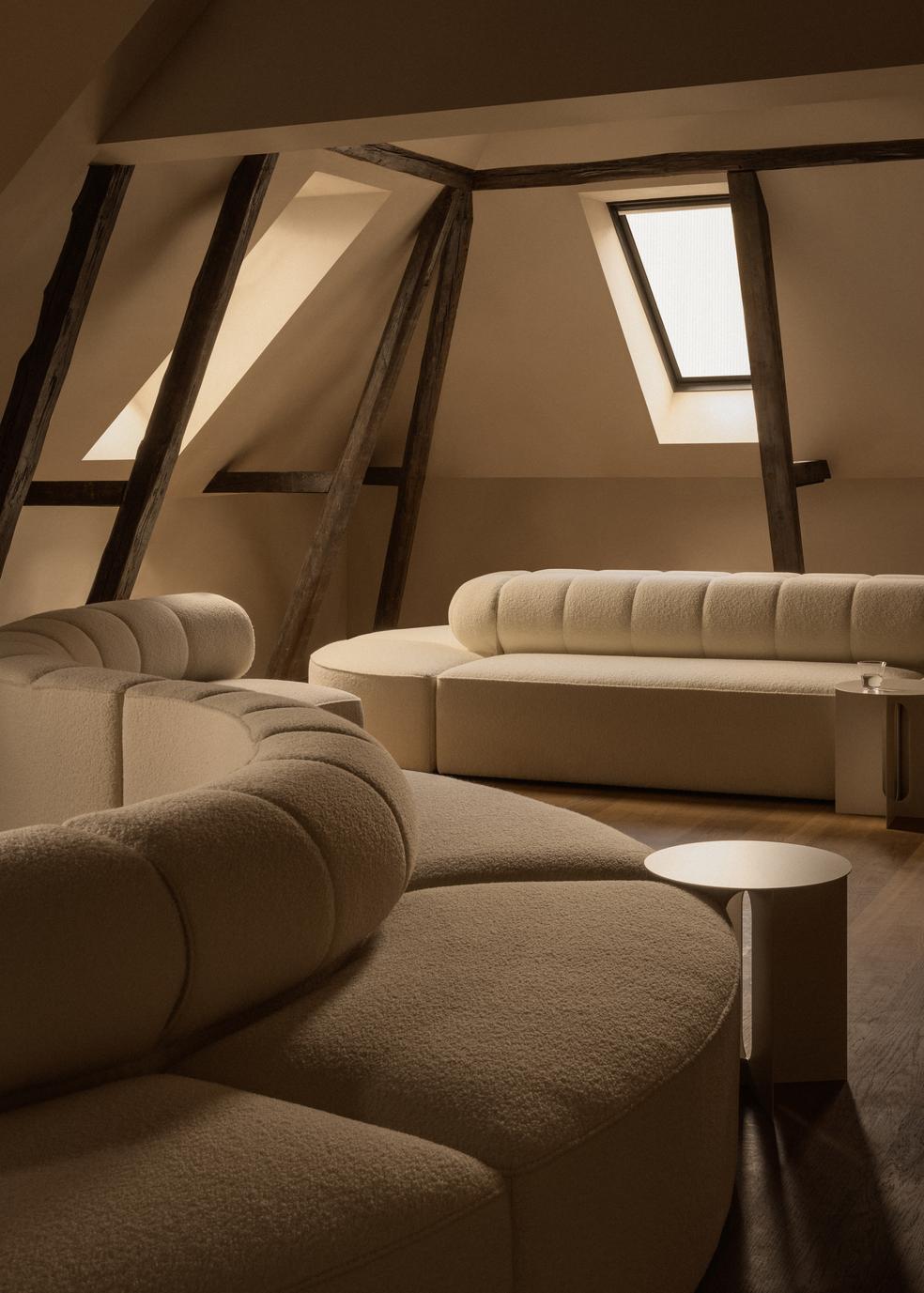 Eave Seamline Modular Sofa in cream bouclé and Androgyne Side Table in an attic room with exposed beams.