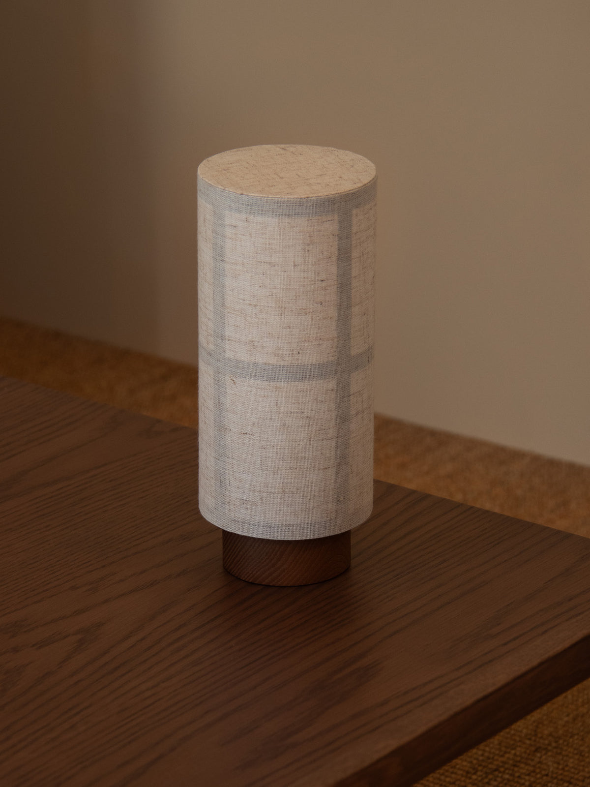 Hashira Table Lamp, Portable, featuring a tactile linen shade standing on a dark wooden lounge table.