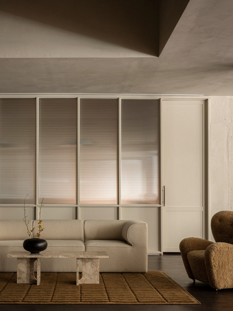 Neutral-toned living room with beige upholstered sofa, marble coffee table, ribbed glass partition and textured brown rug