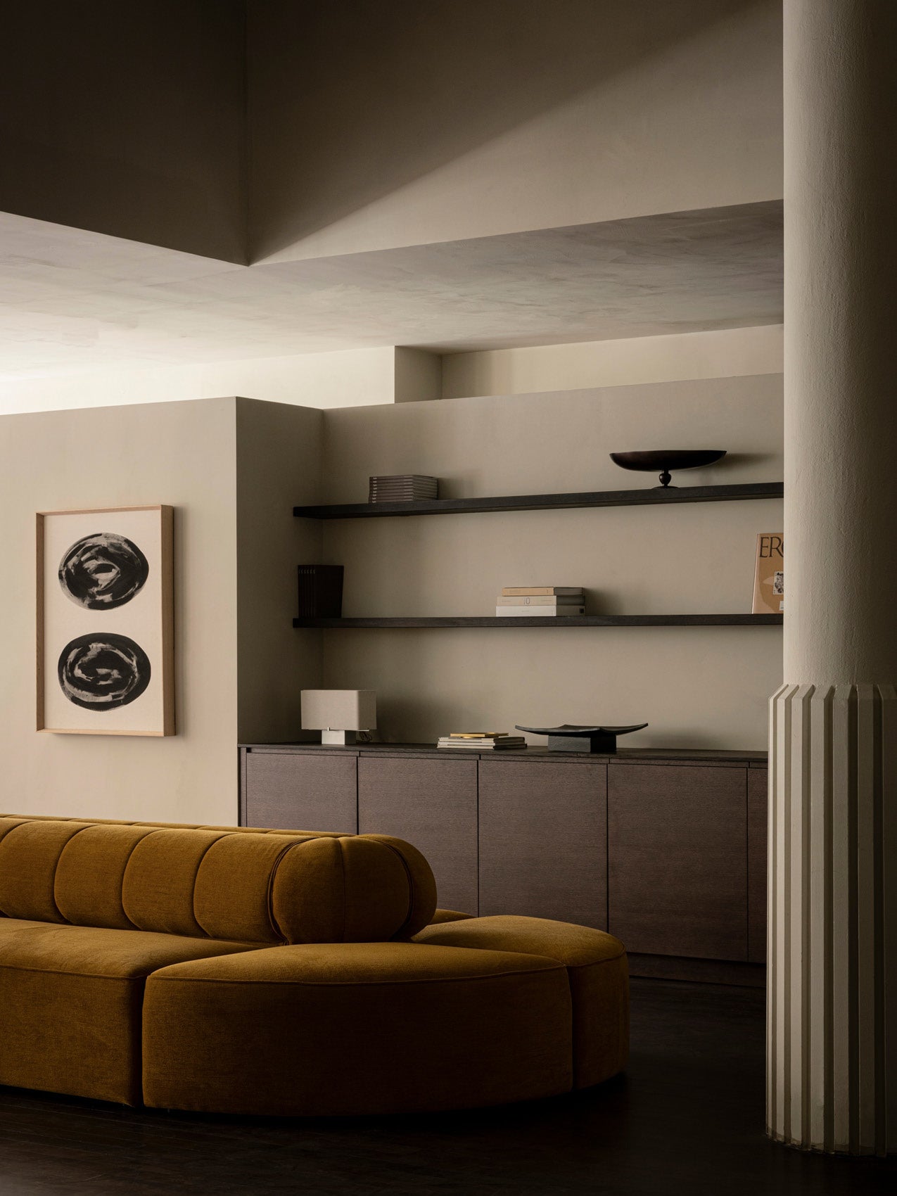 Minimal living room with mustard velvet curved sofa, dark wood cabinet and floating shelves with neutral decor