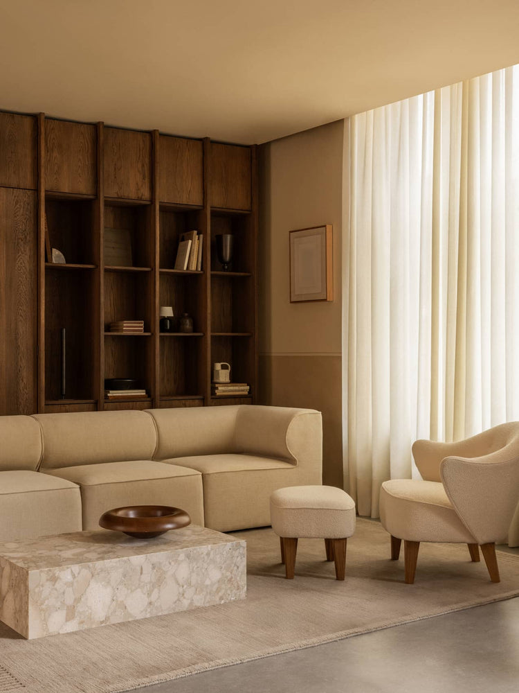 Neutral-toned living room with beige curved fabric sofa, matching armchair and ottoman, marble low table and dark wood
