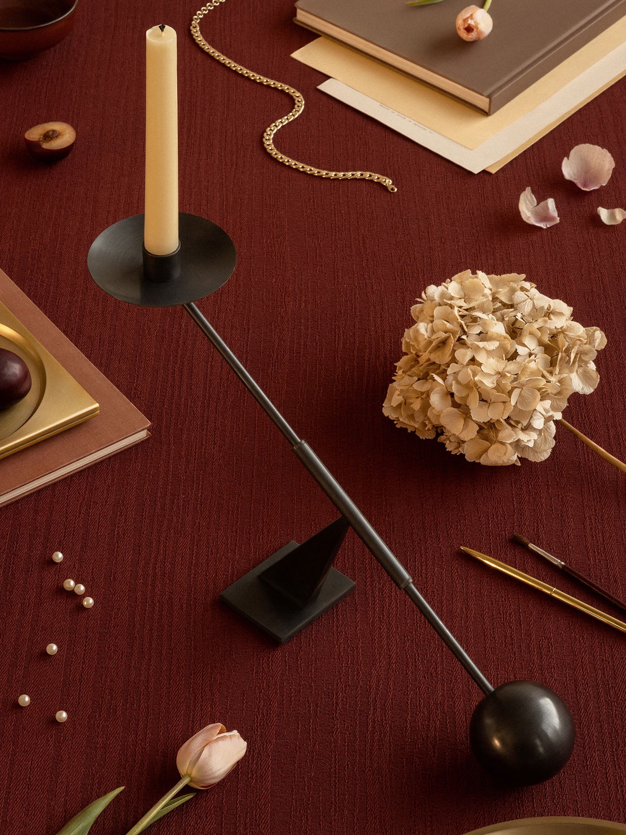 Overhead view of the black Audo Interconnect Candle Holder on a red tablecloth, styled with dried flowers, books and pearls.