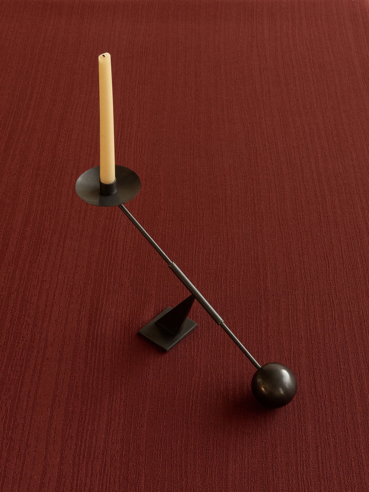 Audo's black metal Interconnect Candle Holder Small with a cream taper candle, shot from above on a rich, textured red cloth.