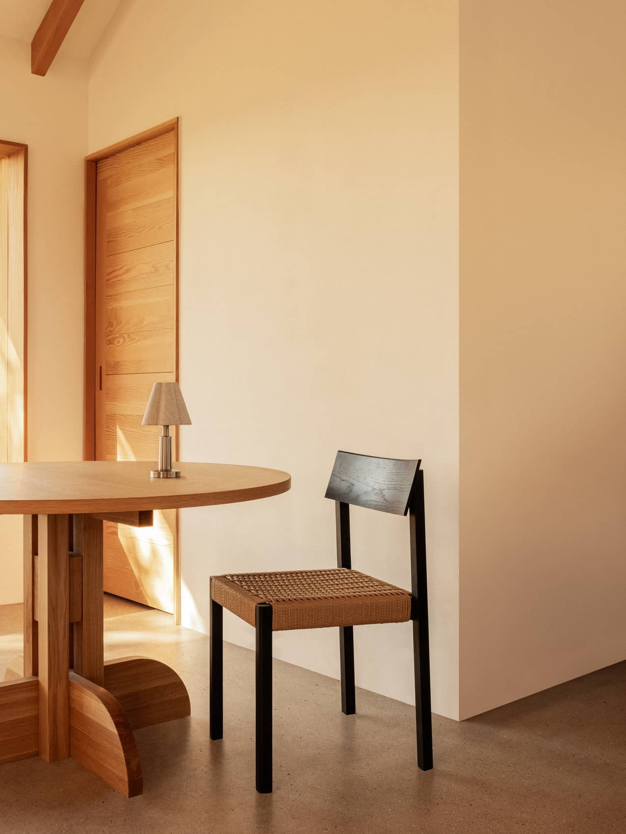 Black Mauro Dining Chair with a paper cord seat beside a Puffin Dining Table and Admiral Portable Table Lamp.
