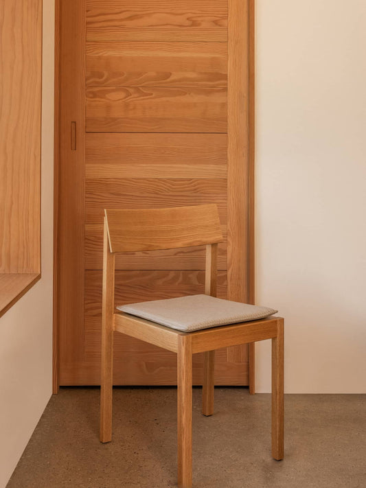 Mauro Dining Chair Seat Cushion in light textile on a wooden Mauro Dining Chair against a warm timber door.