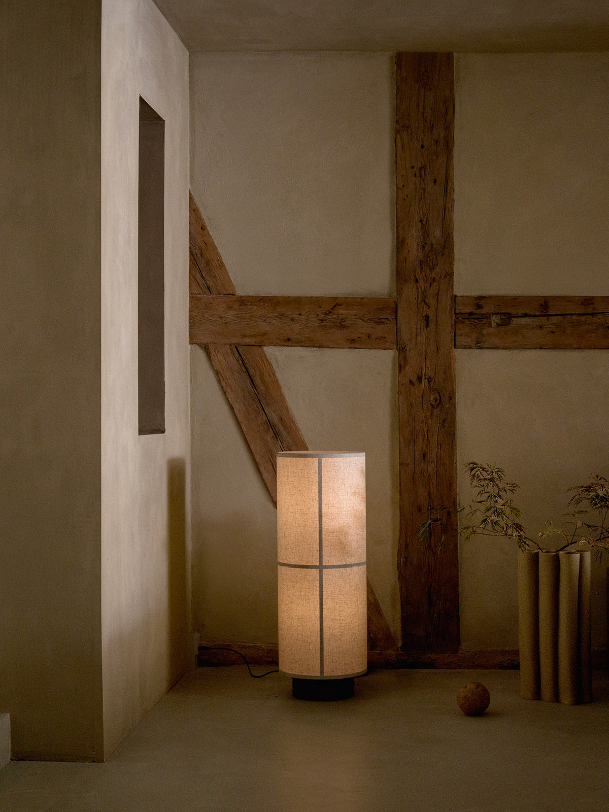 Hashira Floor Lamp, Raw, standing in a rustic room with exposed wooden beams and a warm, glowing linen shade.
