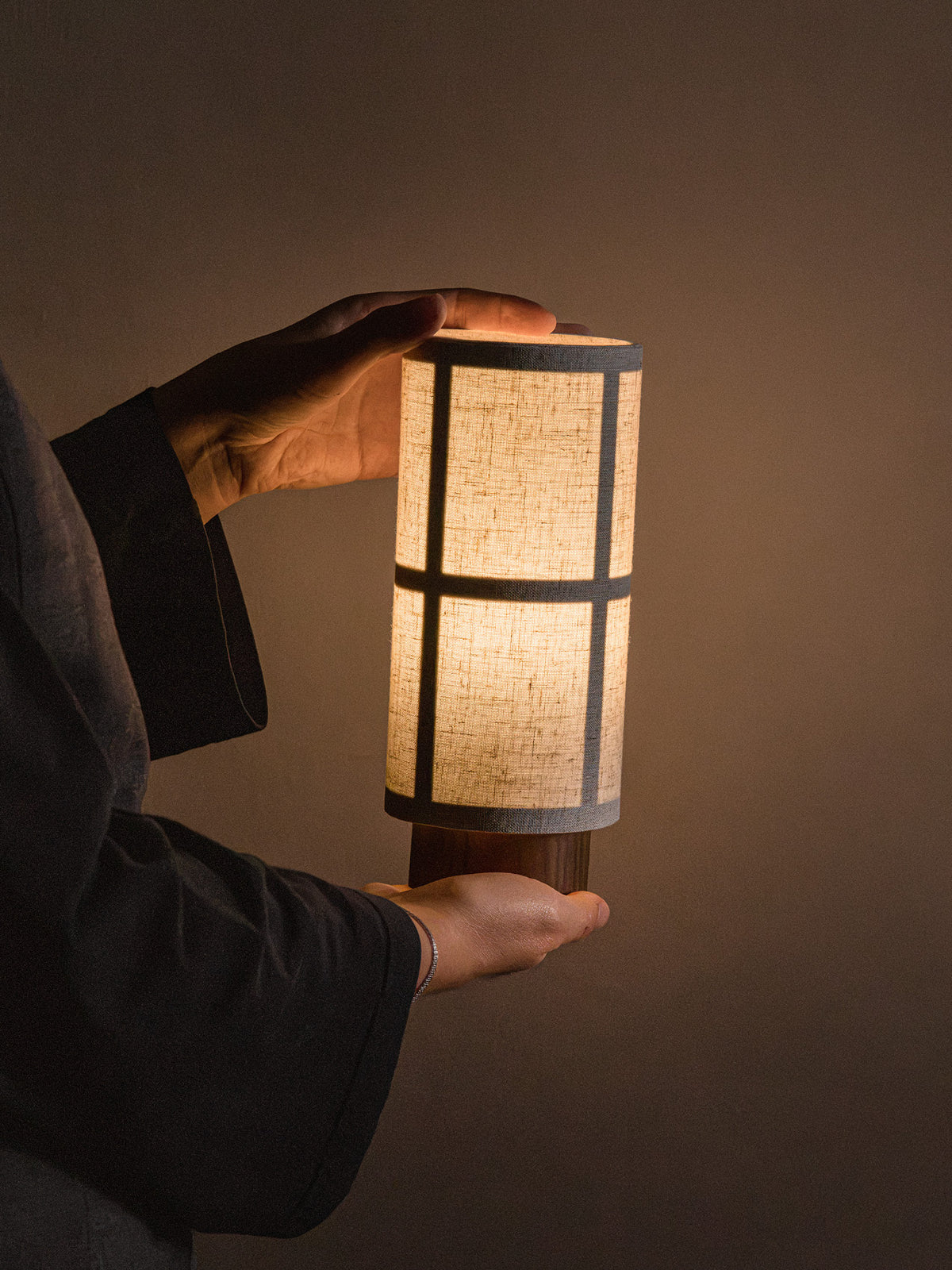 Hashira Table Lamp, Portable, glowing warmly while held in hands, showcasing its tactile linen shade and compact design.