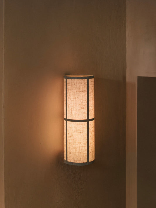 Hashira Wall Lamp in raw slub linen mounted on a dark textured wall, emitting a warm, diffused ambient glow.