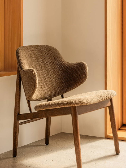 The Penguin Wooden Lounge Chair, fully upholstered in Logan Nutmeg fabric, styled in a minimalist interior corner.