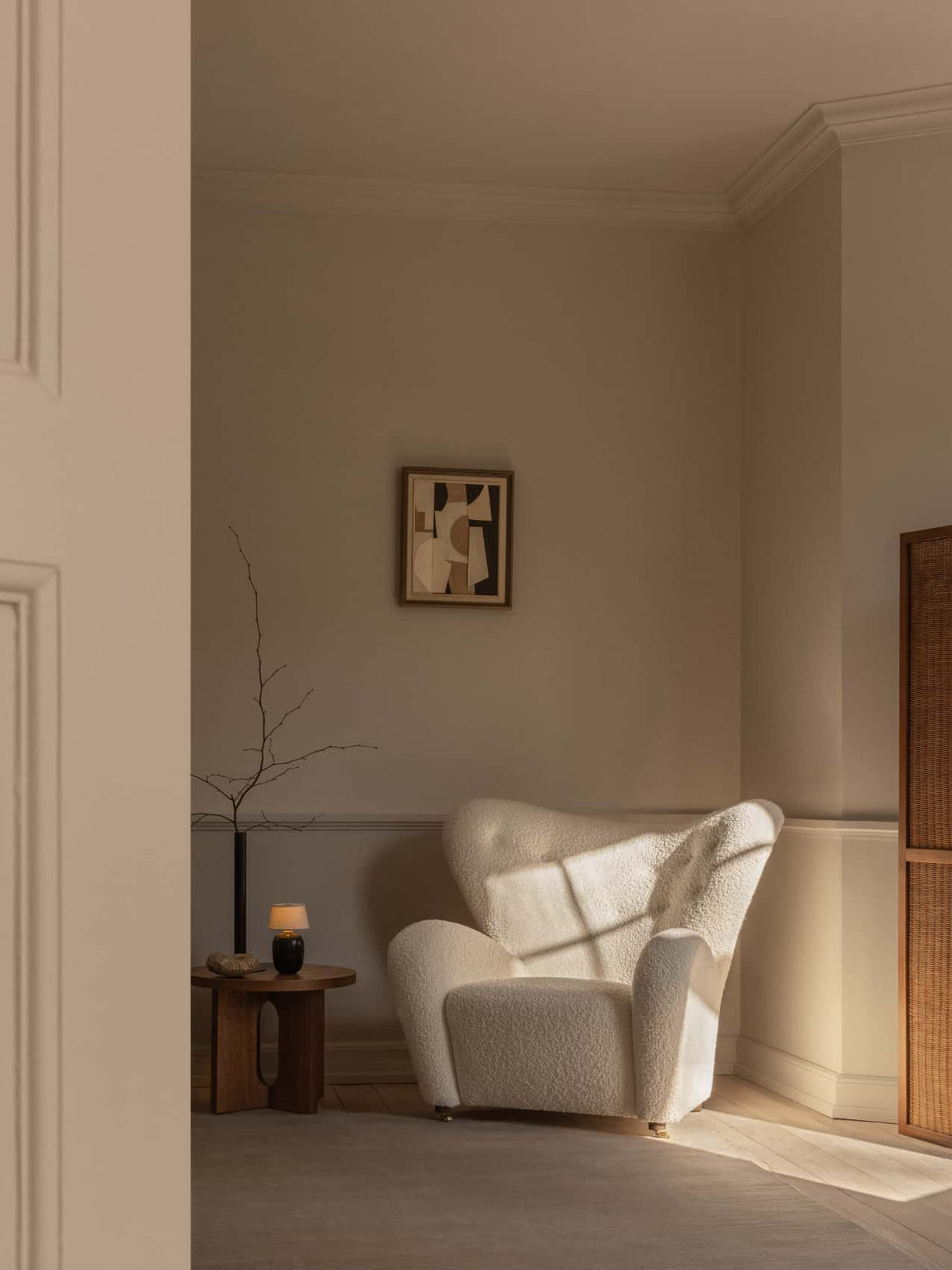 Cream boucle wingback armchair beside a round wooden side table with a