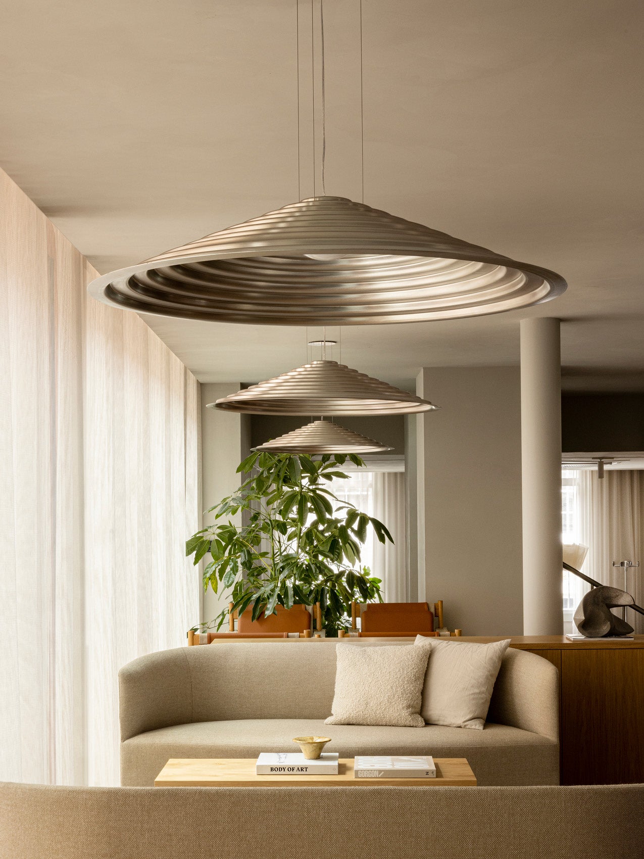 Three brass-toned concentric ribbed pendant lights, saucer-shaped metal shades suspended over a neutral beige living room.