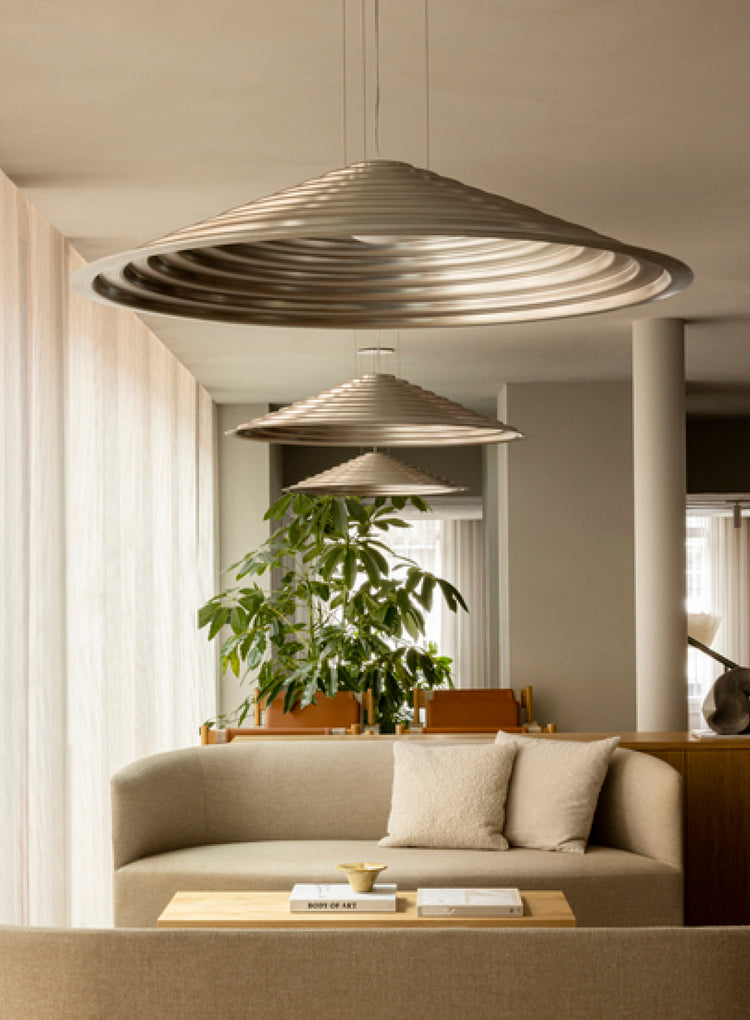 Three concentric, ribbed metal pendant lights in champagne finish hanging above a beige sofa and wooden coffee table.