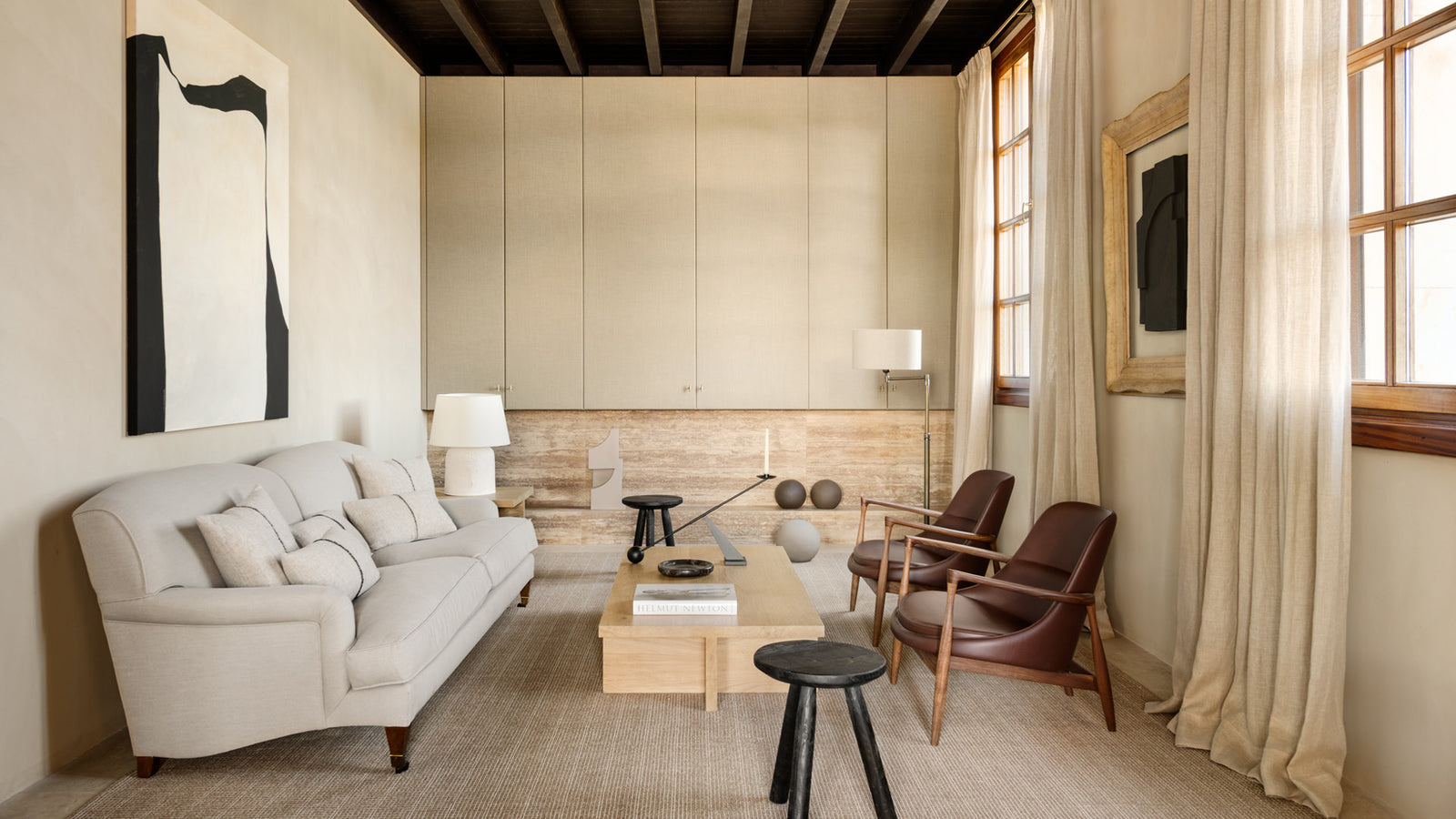 Neutral-toned living room with beige upholstered sofa, wooden coffee table, leather armchairs and soft linen curtains.
