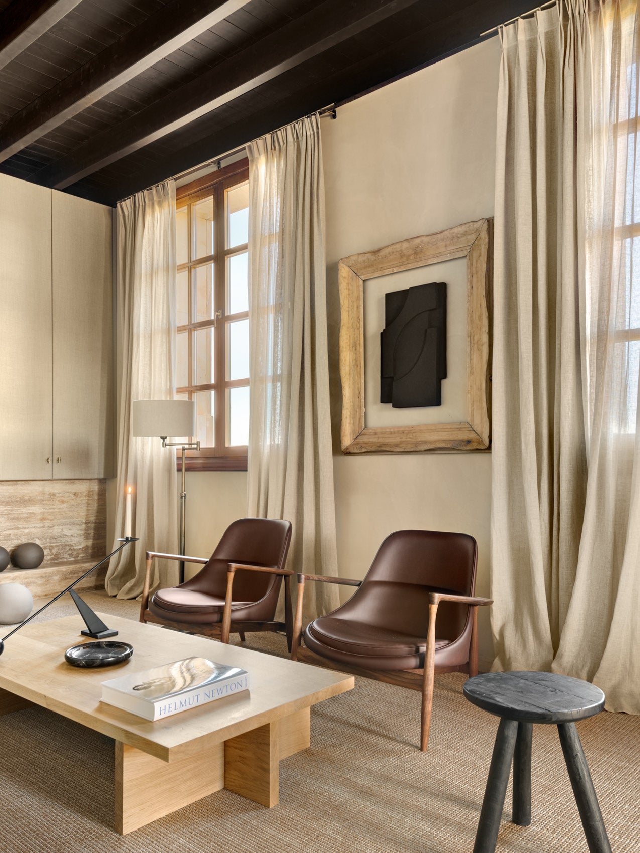 Minimal living room with two brown leather wooden-arm chairs, light oak coffee table, beige linen curtains and framed wall