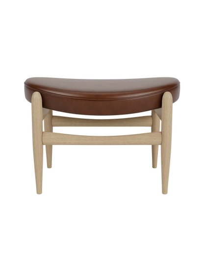 A front view of the Elizabeth Ottoman, featuring a curved brown leather seat and a light natural oak frame.