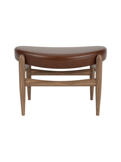 Front view of the Elizabeth Ottoman with a curved brown leather seat and a solid walnut frame on a black background.