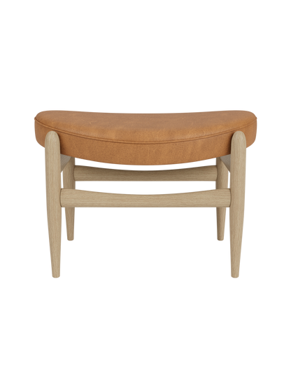 A front view of the Elizabeth Ottoman, featuring a curved seat upholstered in Dunes Cognac leather on a natural oak frame.
