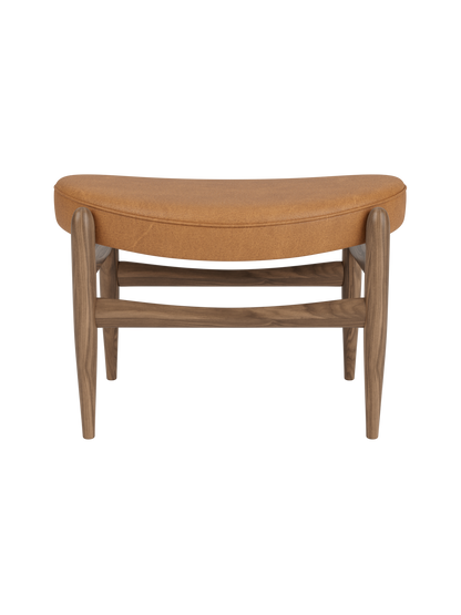 Front view of the Elizabeth Ottoman. The piece has a walnut frame and a curved top cushion upholstered in cognac leather.