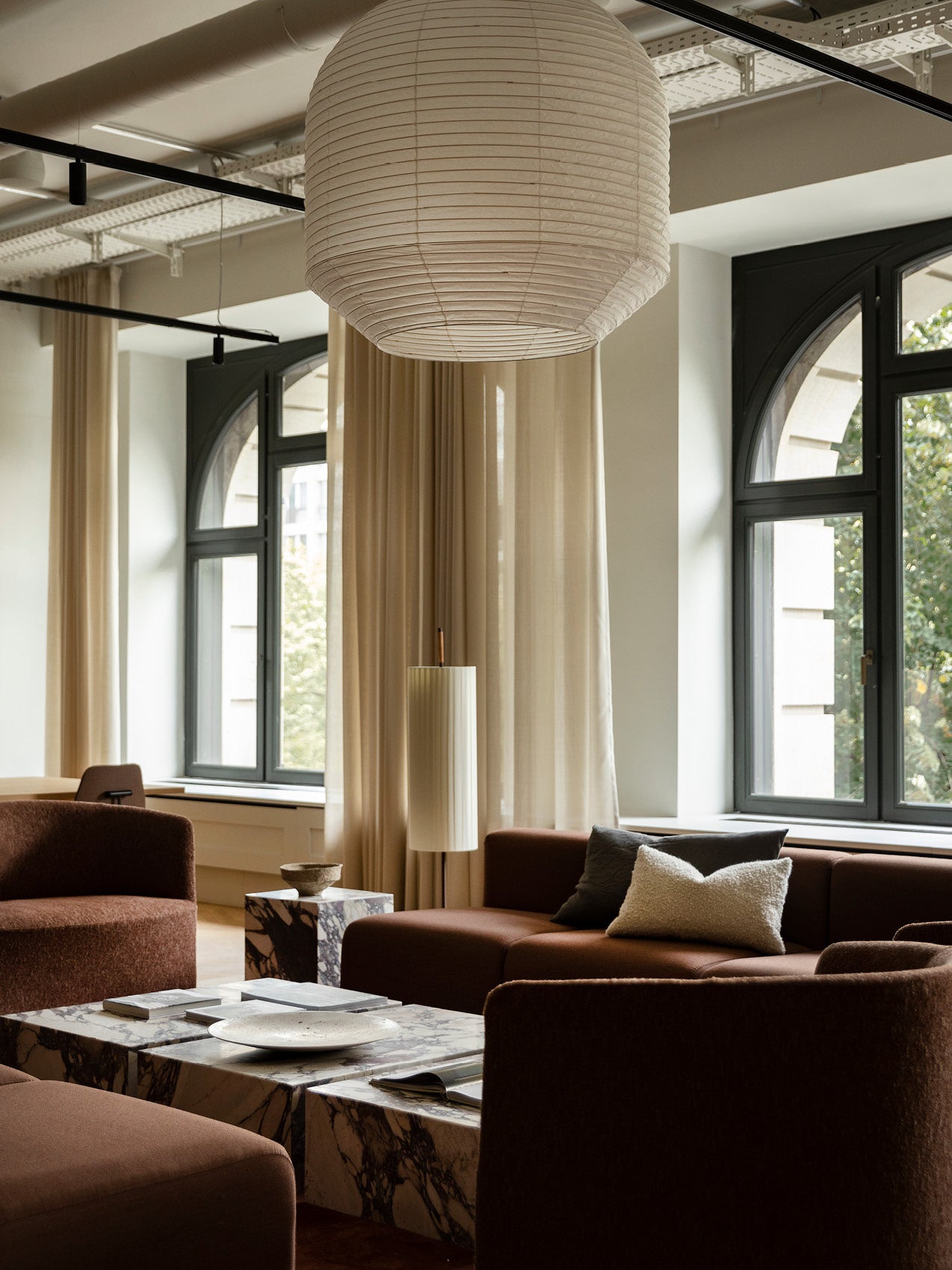 Living room with large round white paper pendant lamp, brown upholstered sofas, marble coffee tables and arched black windows