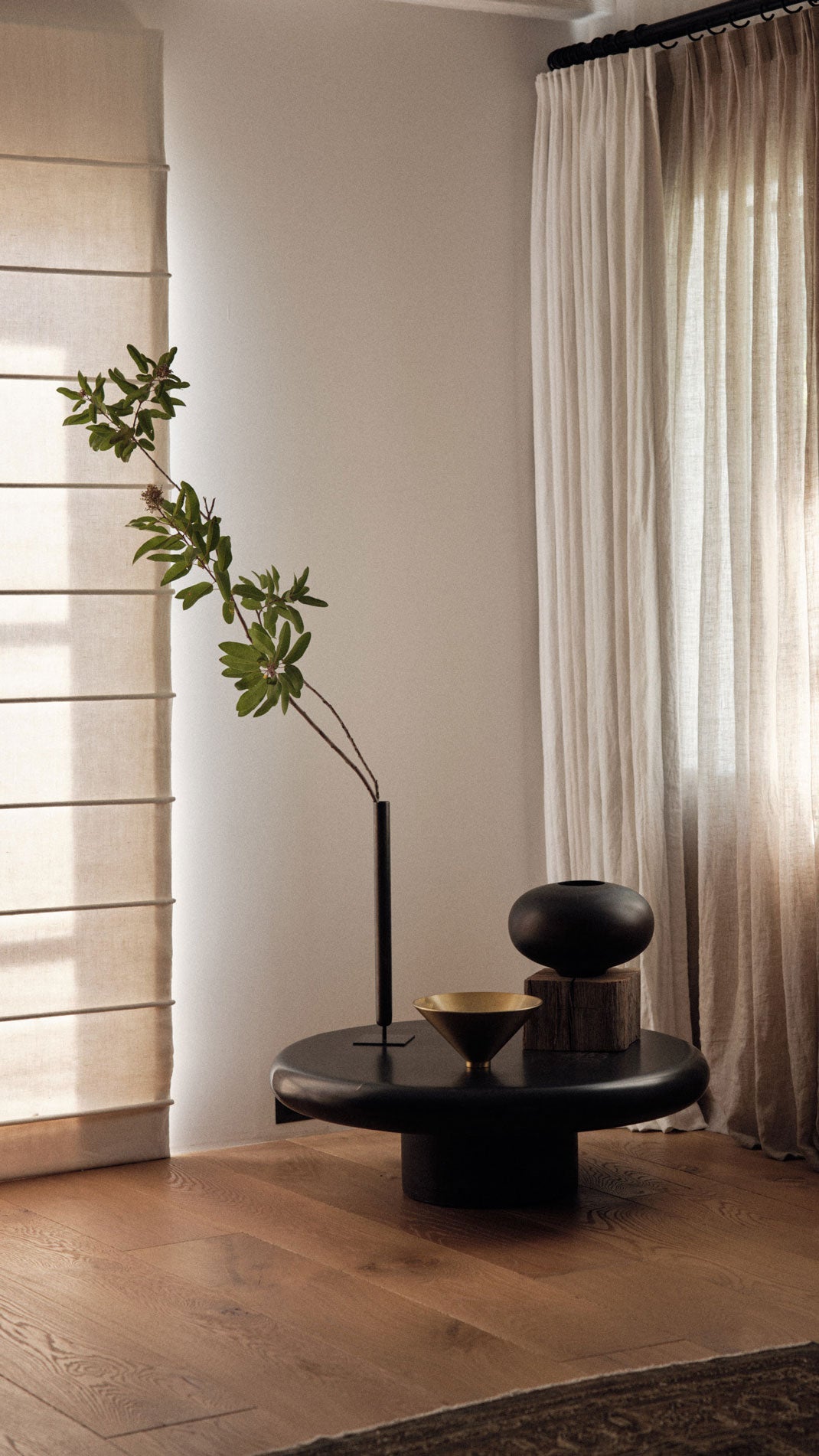 Minimal living room with beige curtains, black round coffee table holding a