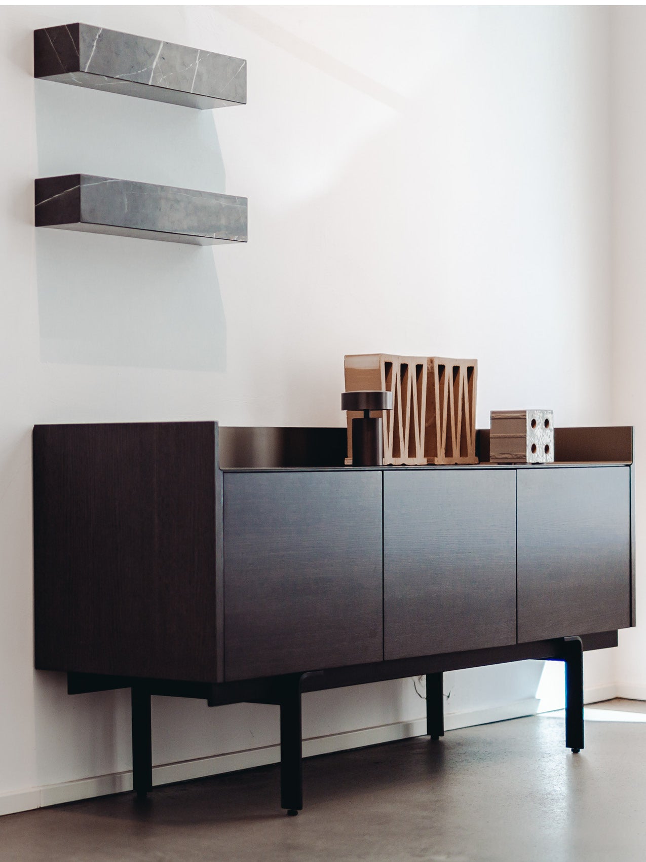 Dark wood wall-mounted sideboard with black legs, two gray marble floating shelves above and small wooden decorative objects