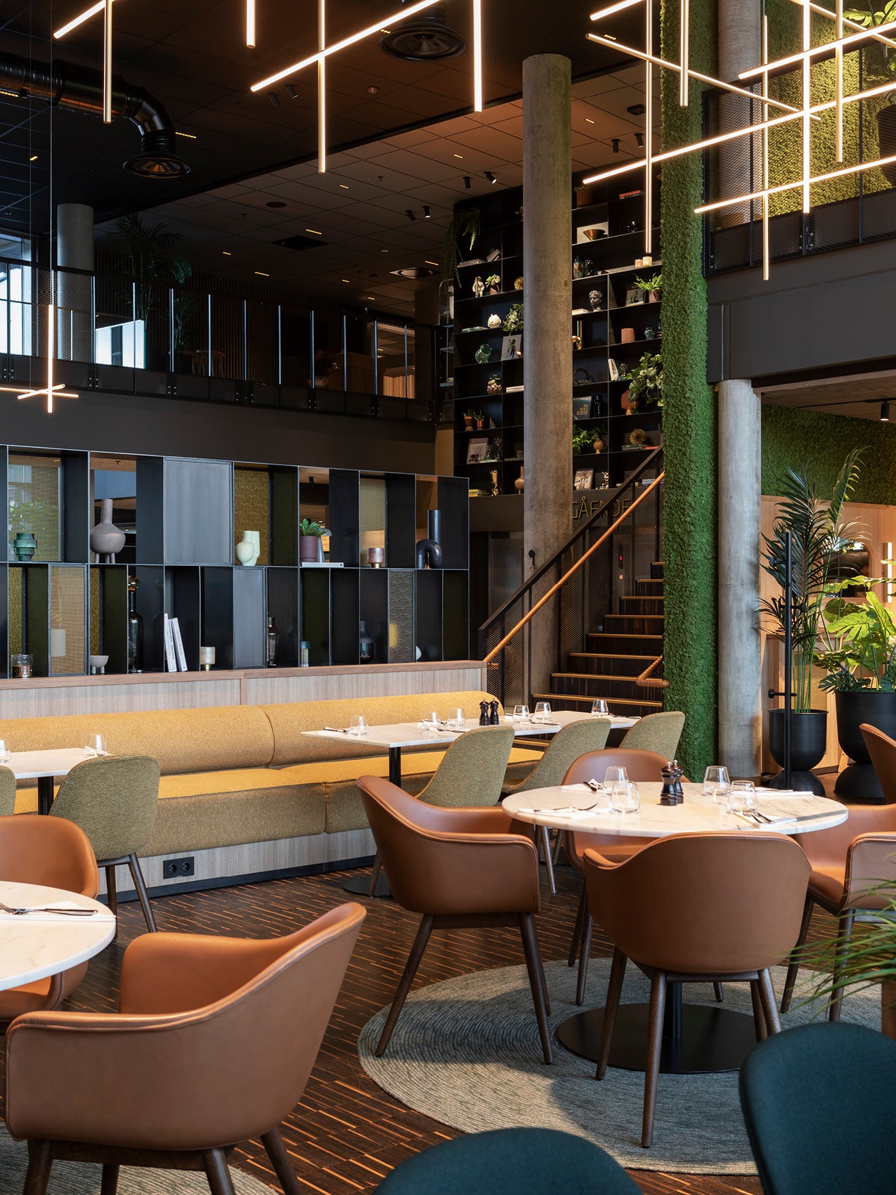 Modern restaurant interior with brown leather chairs, mustard banquette, marble tables, tall concrete columns and linear