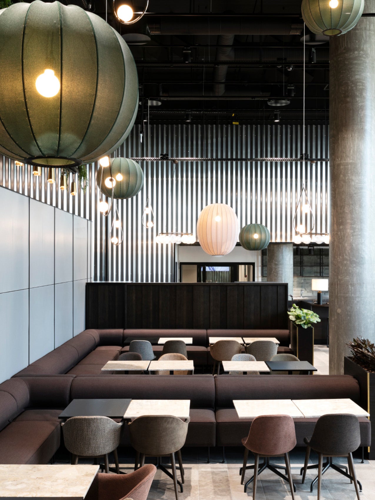 Modern lounge with dark upholstered banquettes, marble-topped tables and oversized green and white fabric pendant lamps