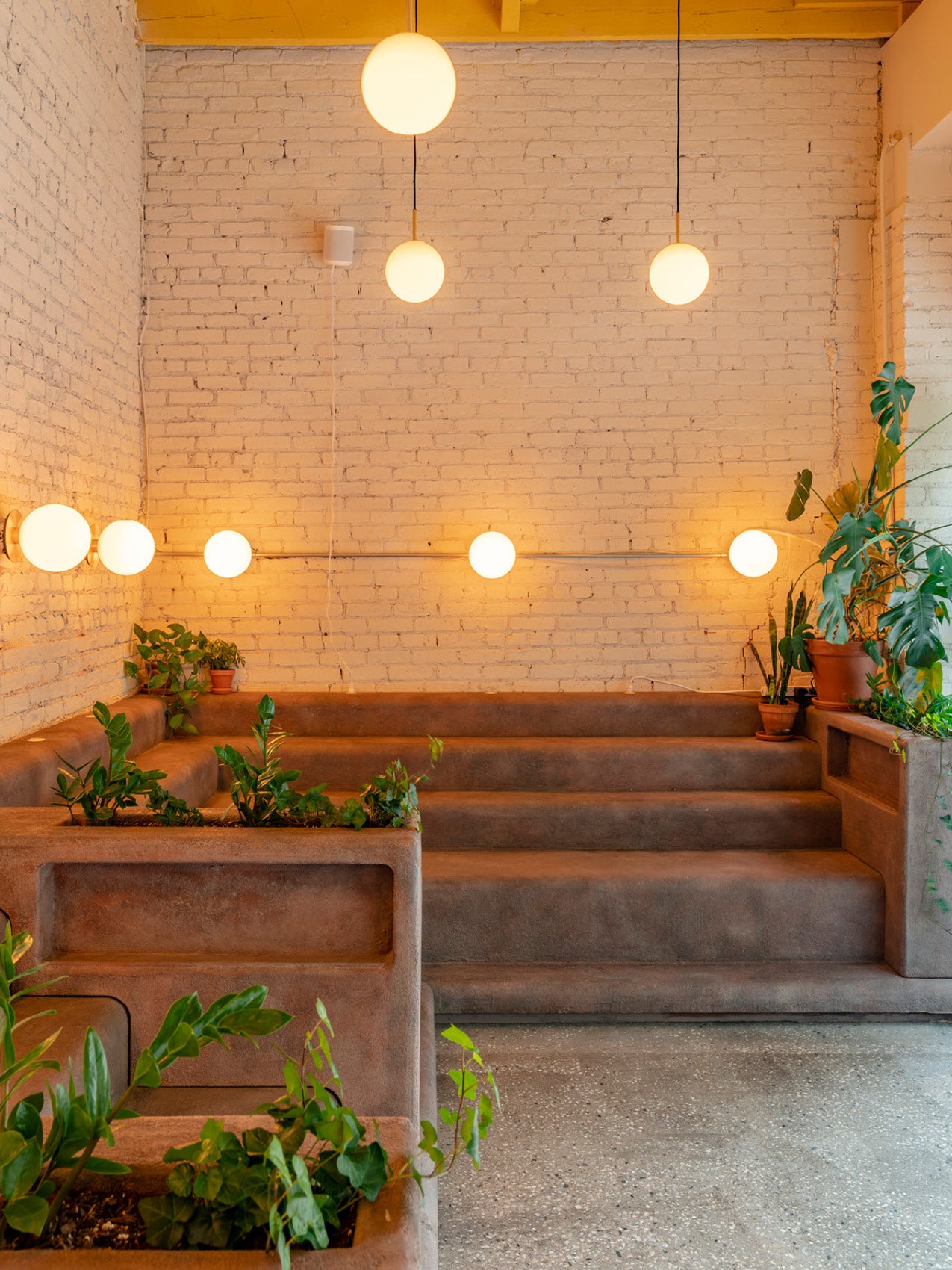 Terracotta stepped seating with built-in planters, white globe pendant and wall lights against painted brick wall