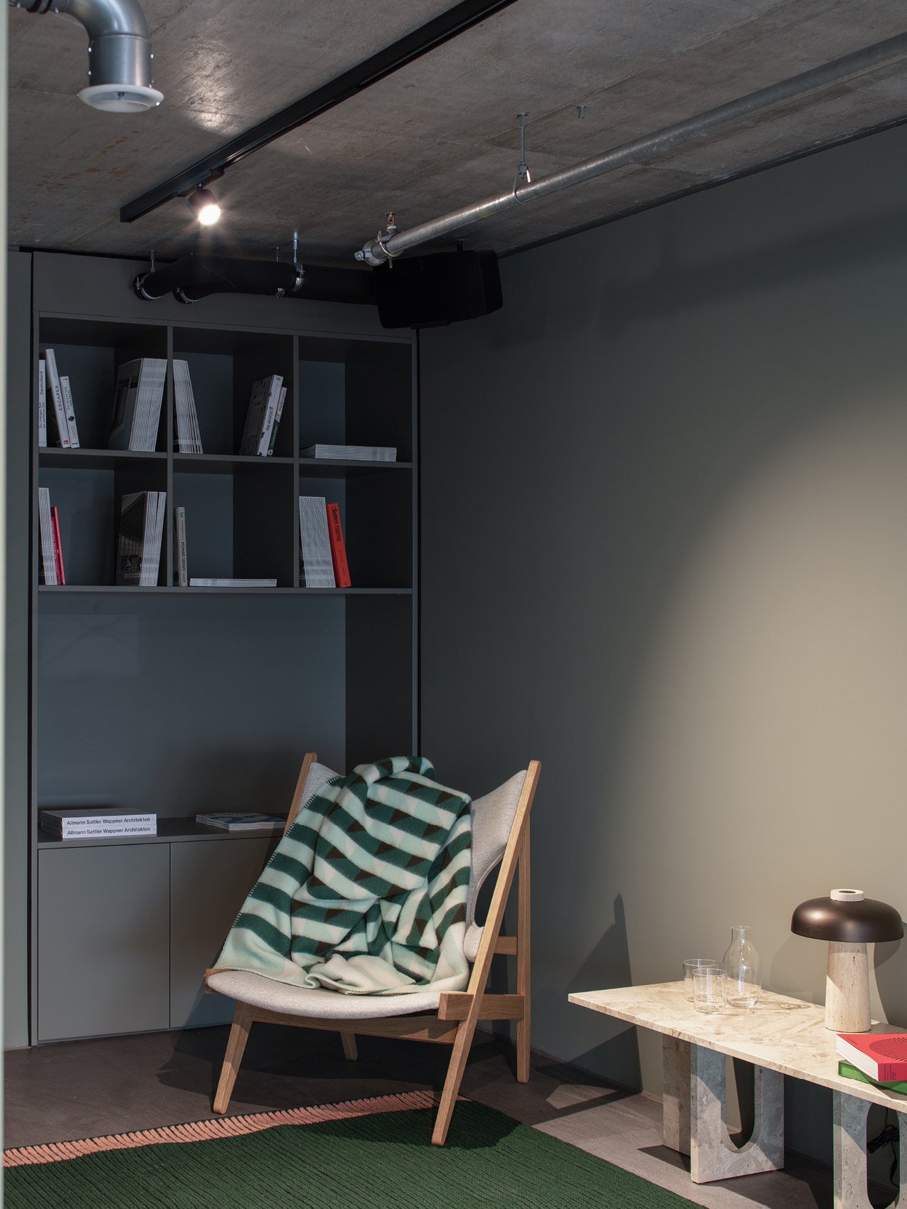 Minimal wooden lounge chair with light grey cushion and green-striped wool blanket beside marble side table and black table